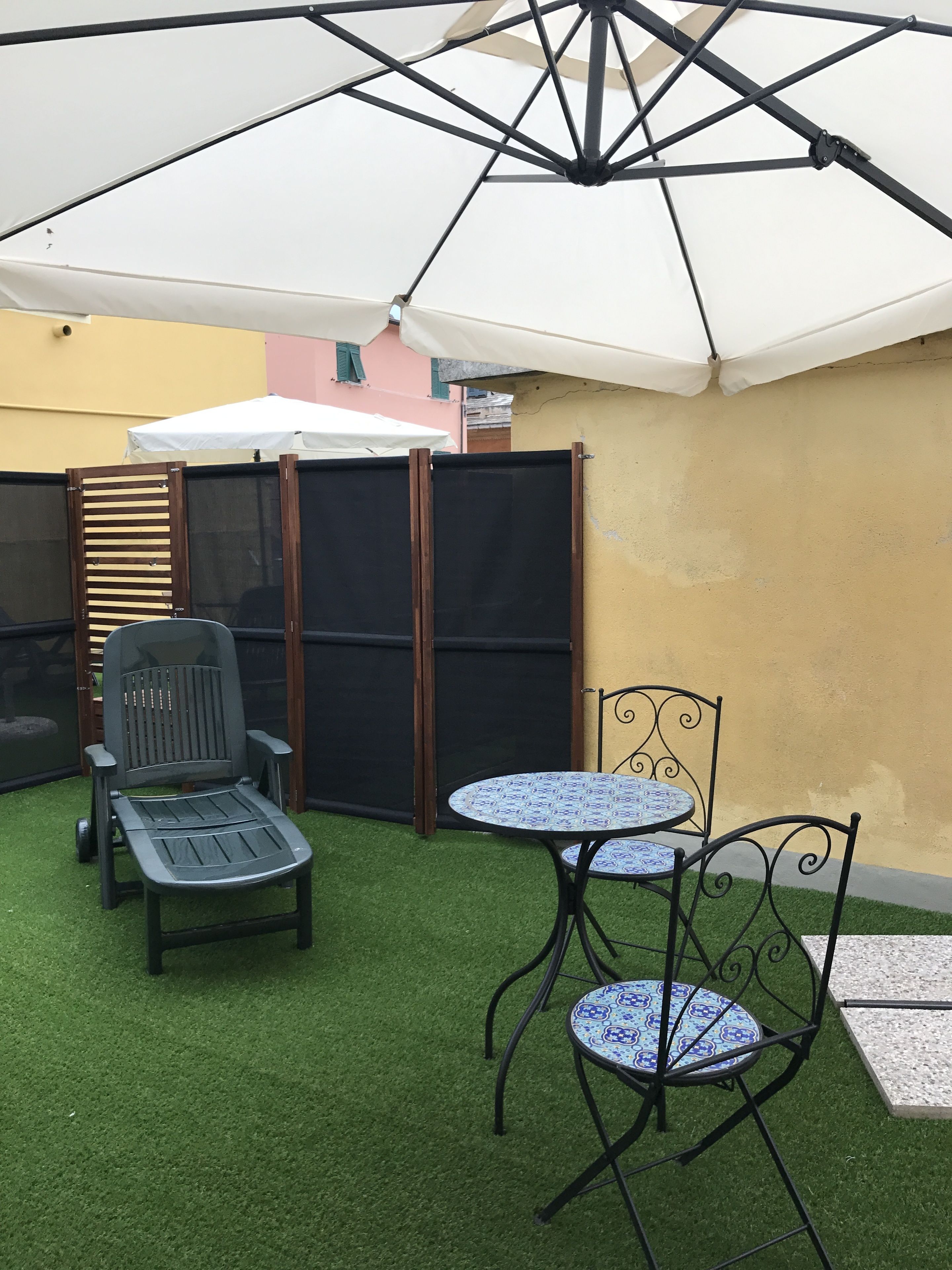 Un área de estar al aire libre con una mesa, sillas y una tumbona, además de un parasol grande.