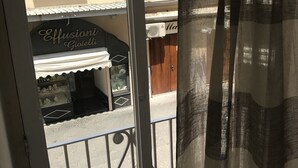 Uitzicht door een balkondeur met metalen hekwerk, een winkel genaamd 