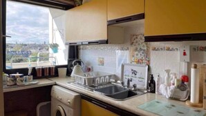 A compact kitchen with a washing machine, a sink, and a window offering a city view. - Aberdeen City Centre Apartment With Private Balcony. (Aberdeen)