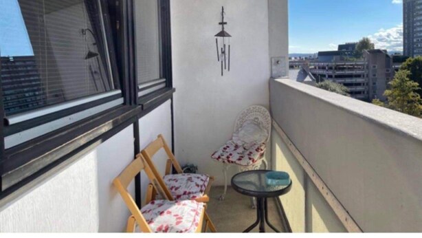 A small balcony with a chair and a table, a window with blinds, and a hanging light fixture. - Aberdeen City Centre Apartment With Private Balcony. (Aberdeen)