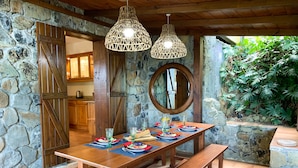 A rustic dining area with a stone wall, wooden bench, and a table set for four.