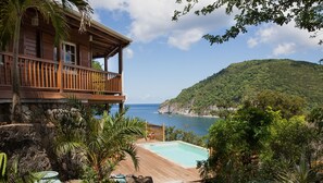 Ein Holzhaus mit Balkon mit Blick auf ein klares, blaues Meer und einen üppigen, grünen Hügel.
