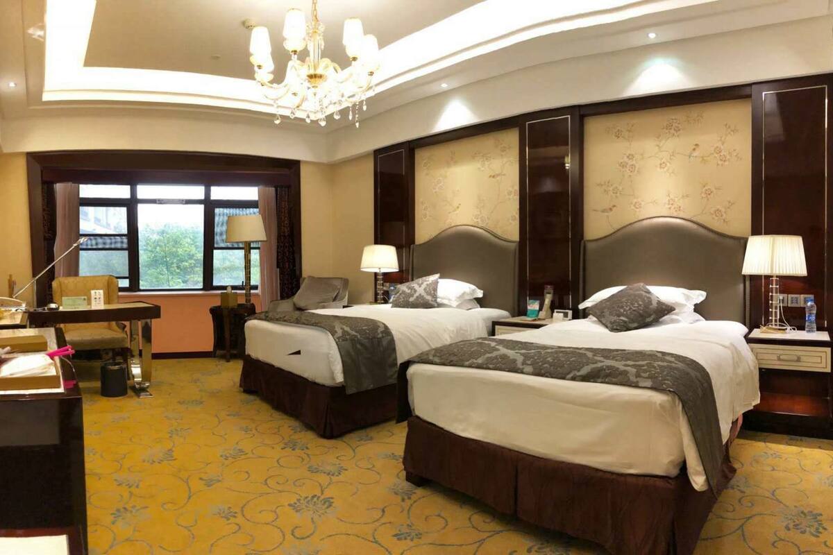 A hotel room with two beds, a desk, a TV, and a large window.