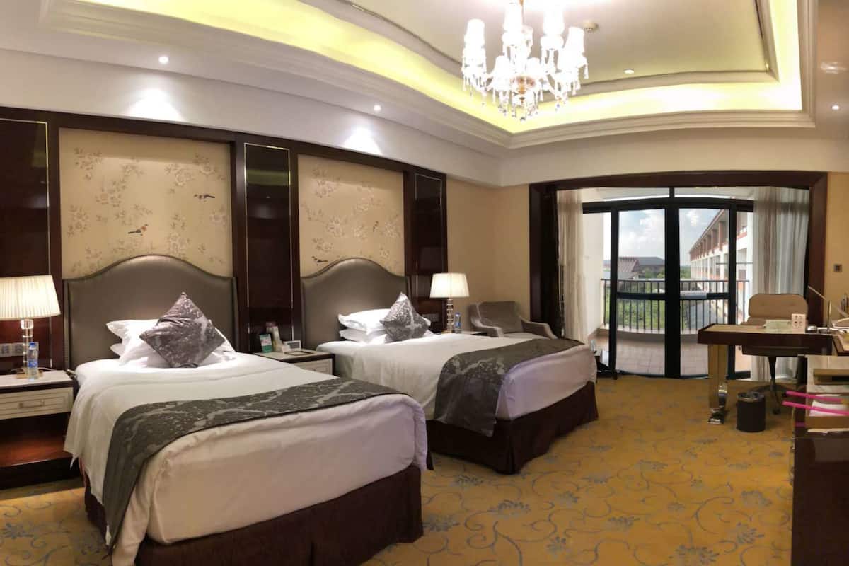 A hotel room with two beds, a desk, a television, and a balcony with a view.