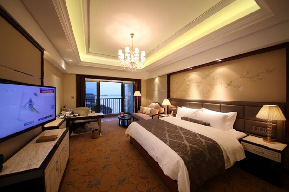 A hotel room with a large bed, a TV, a desk, and a balcony with a view.