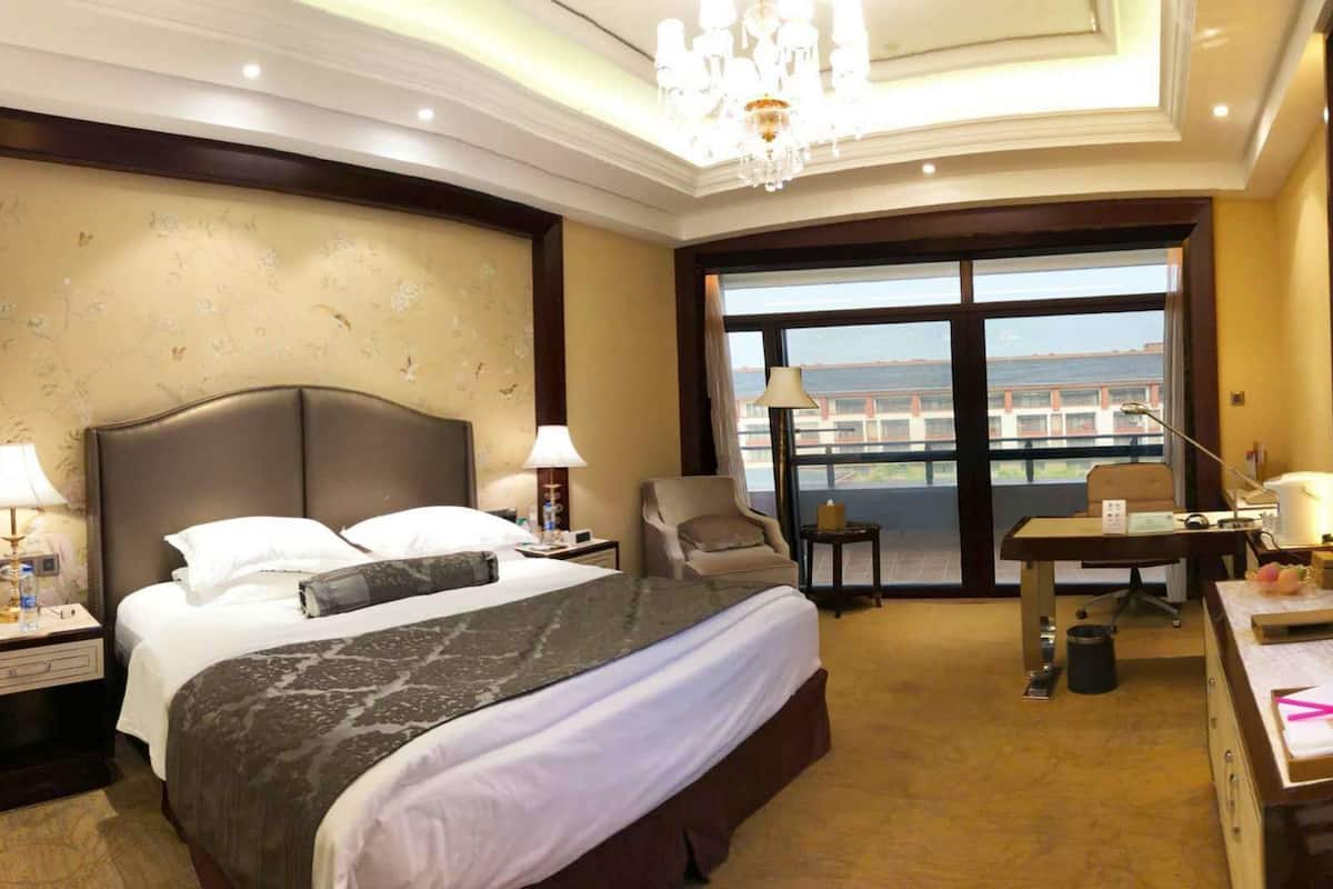 A hotel room with a large bed, a desk, a chair, a television, and a view of the city through the window.