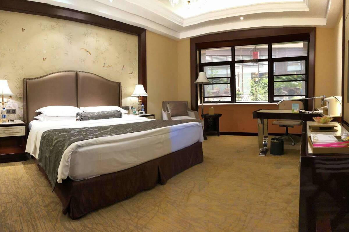 A hotel room with a large bed, two bedside tables with lamps, a desk with a chair, a window with a view, and a TV on the wall.
