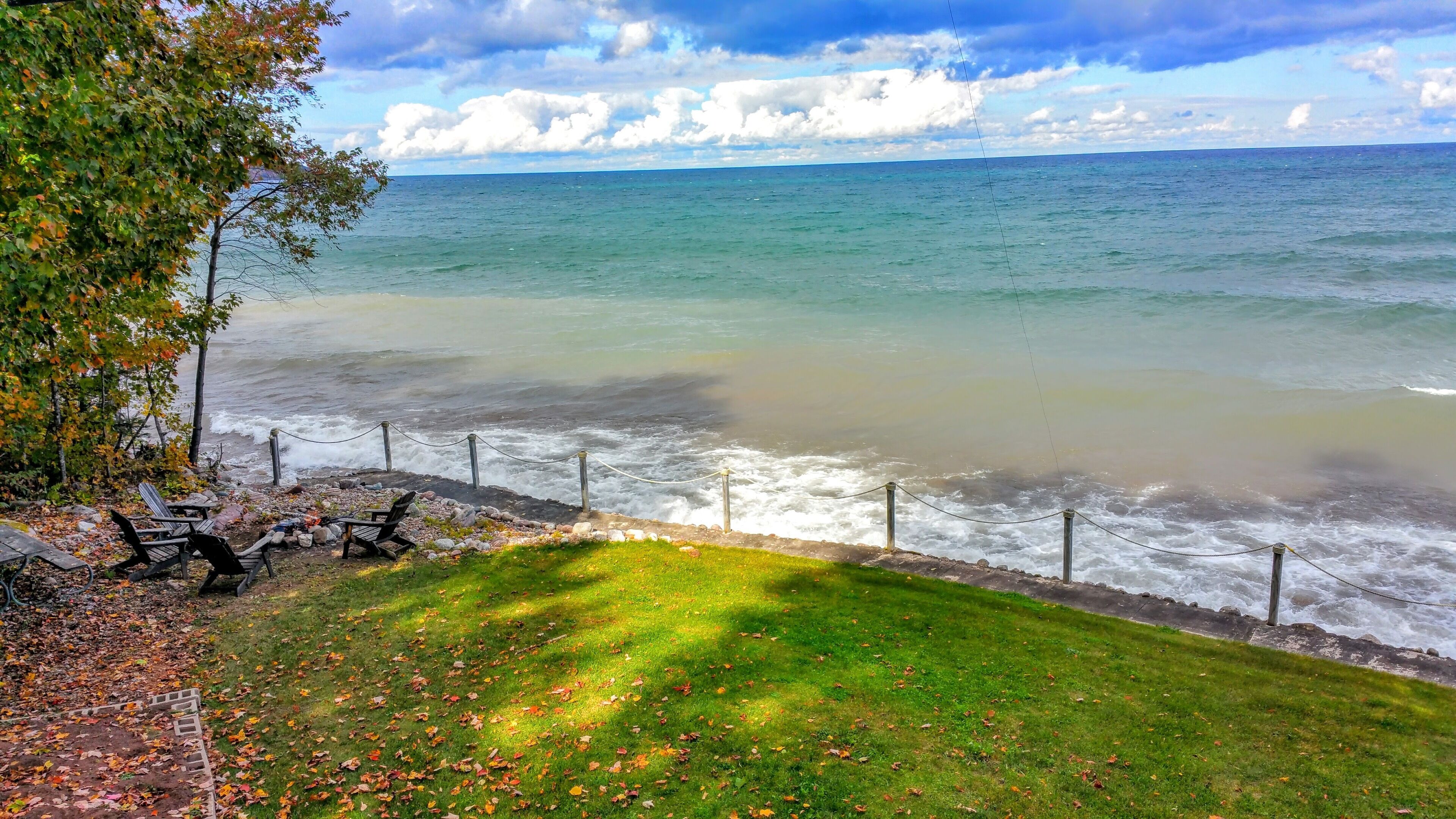 Une vue d’une plage avec une zone herbeuse, des chaises, une rambarde et un ciel nuageux.
