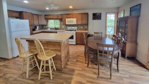 Una cocina con armarios de madera, un refrigerador, una estufa, un microondas y un comedor con sillas y una mesa de madera.