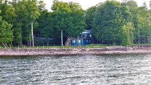 Una cabaña junto al lago con un muelle, rodeada de un bosque frondoso.
