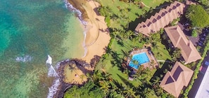 Vue aérienne d’un complexe hôtelier doté d’une plage, d’une piscine et de plusieurs bâtiments aux toits distinctifs.