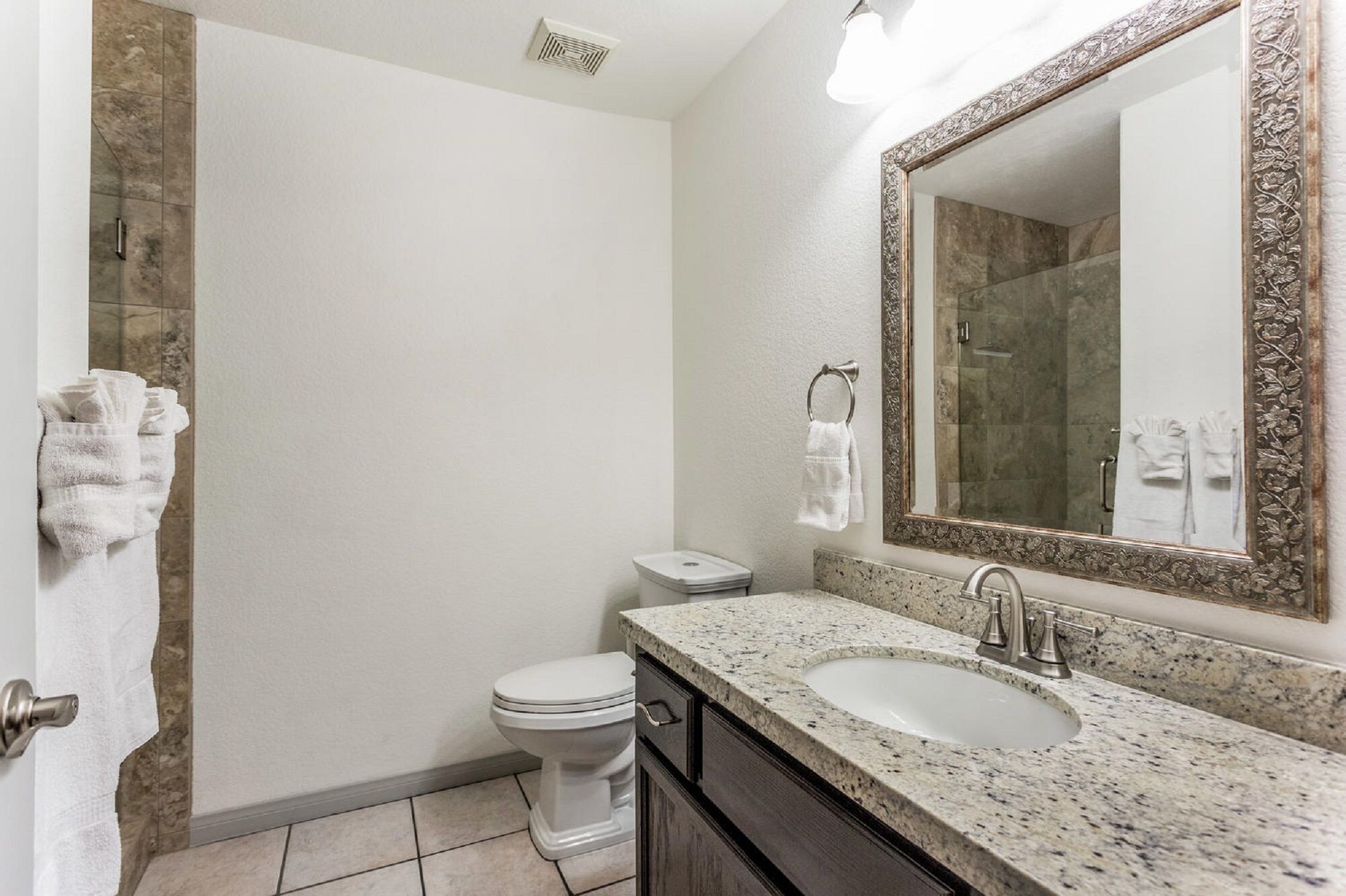 Une salle de bain équipée de toilettes, d’un lavabo et d’un grand miroir orné d’un cadre travaillé.
