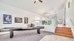 Une pièce spacieuse équipée d’une table de billard, ornée d’œuvres d’art encadrées et dotée d’un escalier menant à un autre niveau.