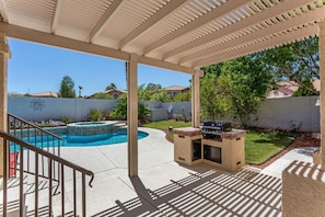 Um alpendre coberto com piscina, área de churrasco e vista para o quintal.