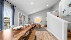 A modern living room with a wooden dining table, a sofa, and a staircase.