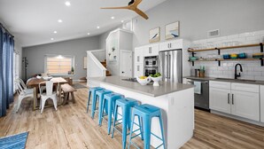 A modern kitchen with white cabinets, a central island with stools, a ceiling fan, and a dining area with a wooden table and chairs.