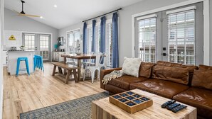 A modern living room with a brown leather sofa, wooden coffee table, and a dining area with a wooden table and chairs.