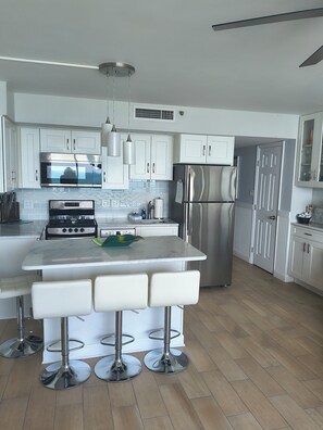 A modern kitchen with white cabinets, stainless steel appliances, a central island with bar stools, and a tiled backsplash.