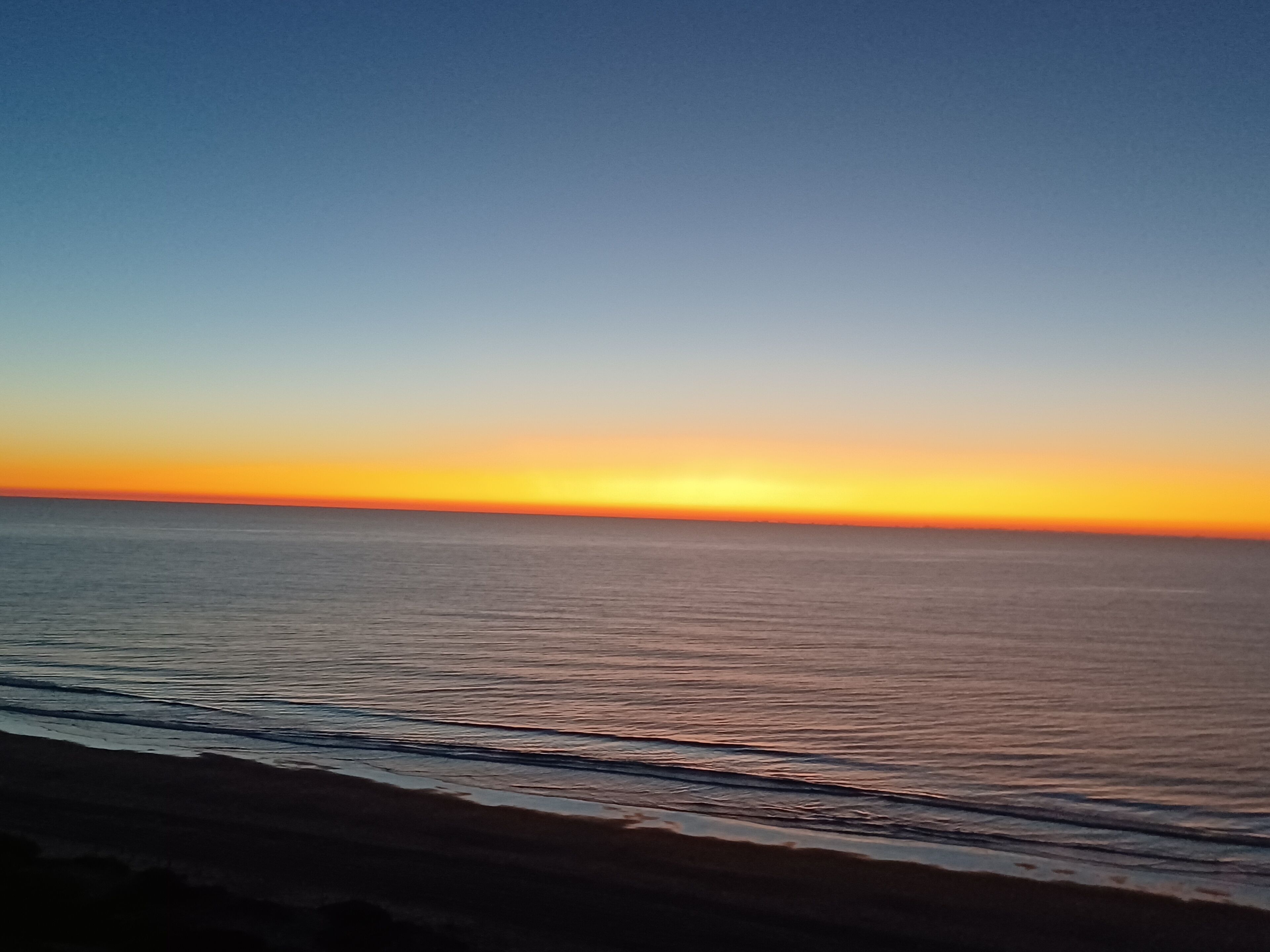 Une plage au coucher du soleil, avec une eau calme et un ciel dégagé.