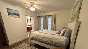 Ein Schlafzimmer mit Bett, Deckenventilator, Nachttisch, kleinem Tisch, Teppich und einem Bild an der Wand.