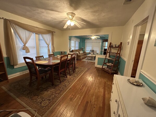 Un coin repas avec une table et des chaises en bois, un ventilateur de plafond et une vue sur le salon.