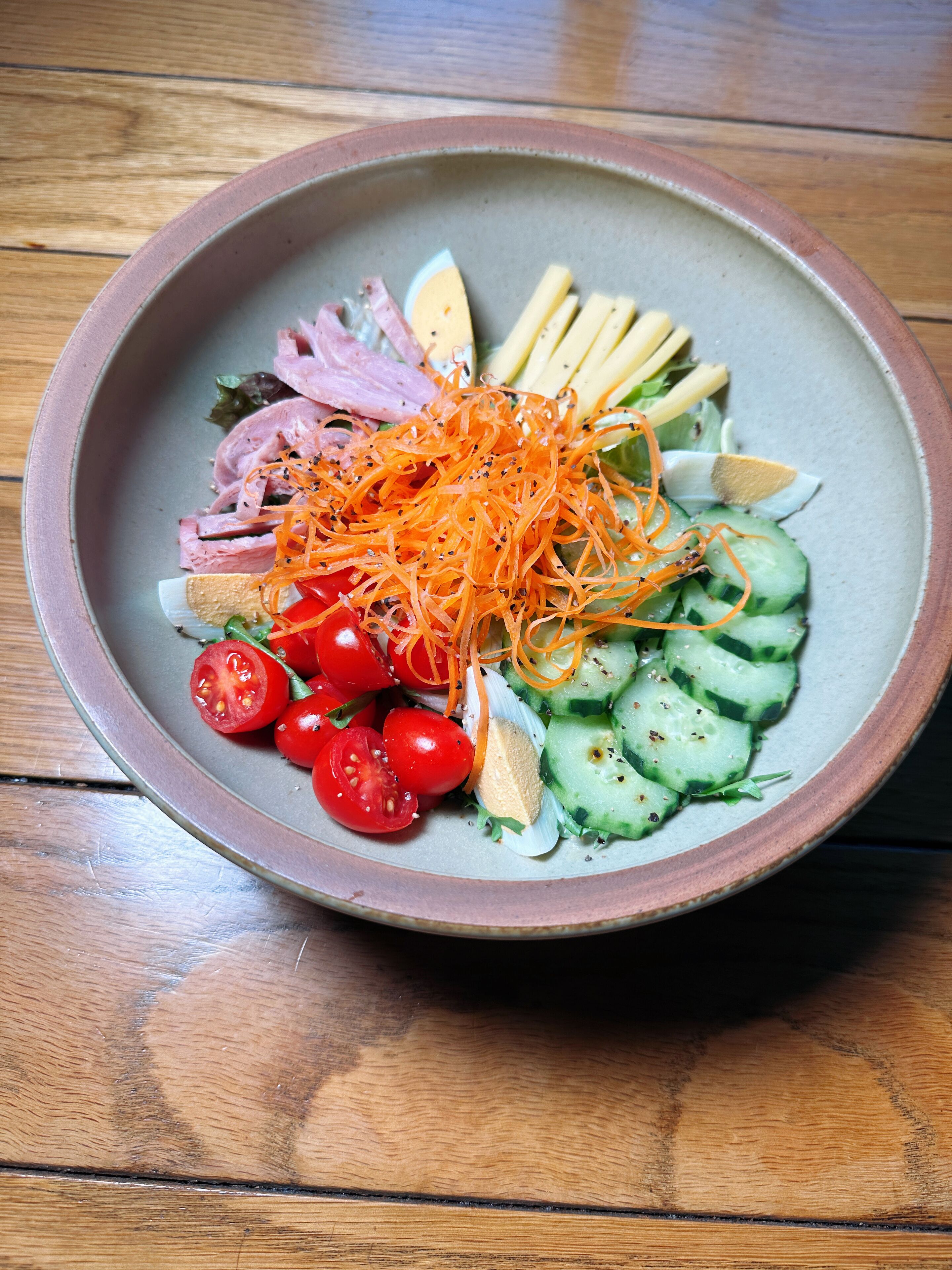 Un saladier rempli de salade, avec divers légumes et de la viande, posé sur une table en bois.
