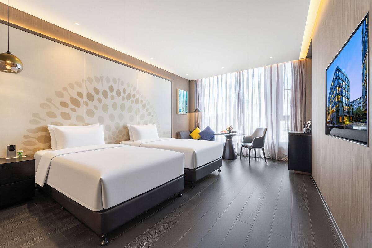 A hotel room with two beds, a desk, a chair, and a large window with curtains.