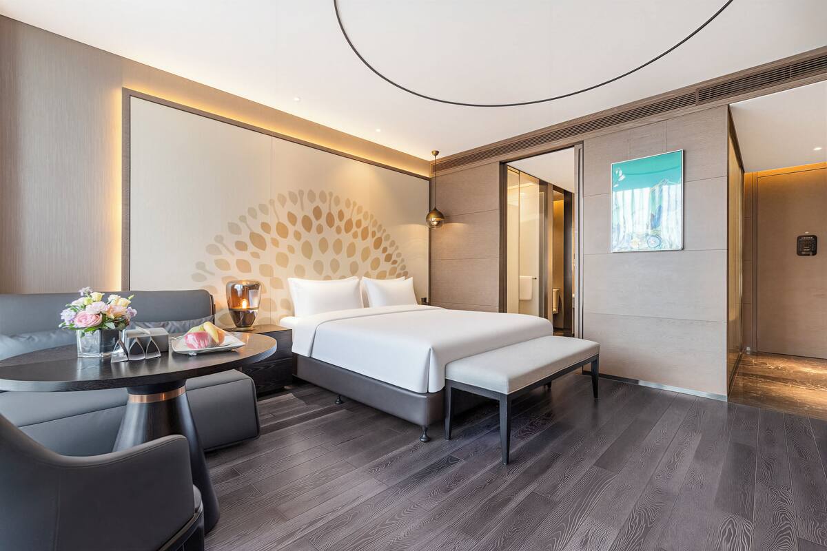 A modern hotel room with a bed, bedside table, and a seating area with a table and chairs.
