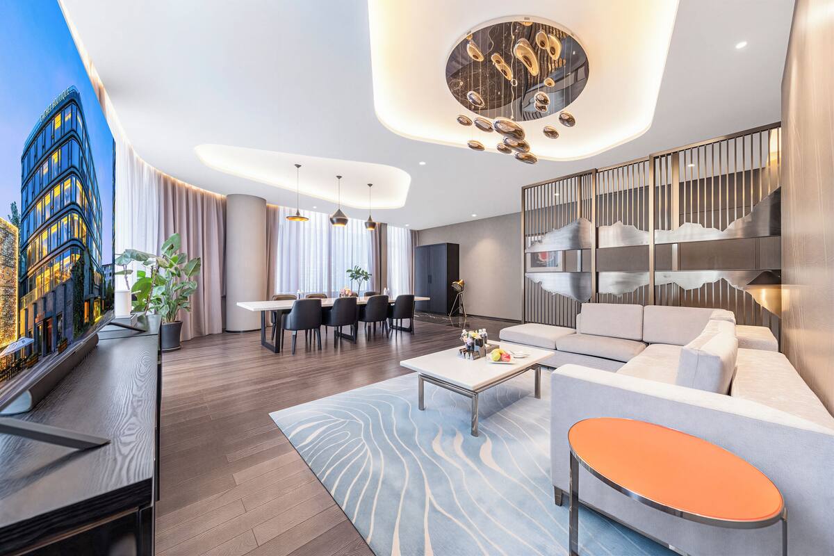 A modern hotel lobby with a dining area, a sofa, a coffee table, and a view of a building.