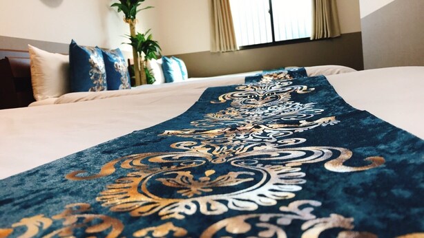 Una cama con un corredor estampado en azul y dorado, una planta en maceta y una ventana con cortinas.