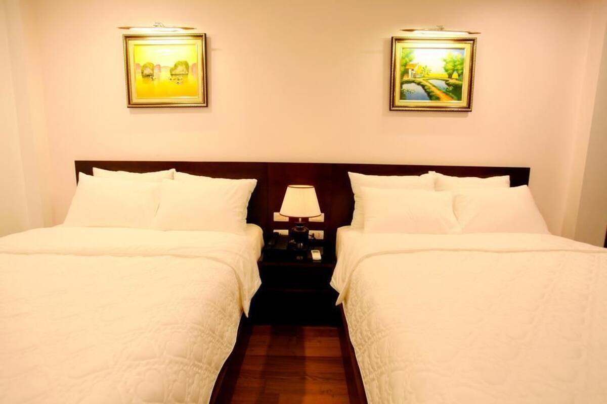 Habitación de hotel con dos camas, una mesita de noche con lámpara y dos cuadros en la pared.