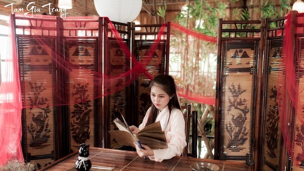 A traditional wooden room with a table, a decorative screen, and a person reading a book. - Camellia Hotel (Ninh Binh)