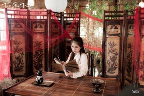 A traditional wooden room with a table, a decorative screen, and a person reading a book. - Camellia Hotel (Hoa Lu)