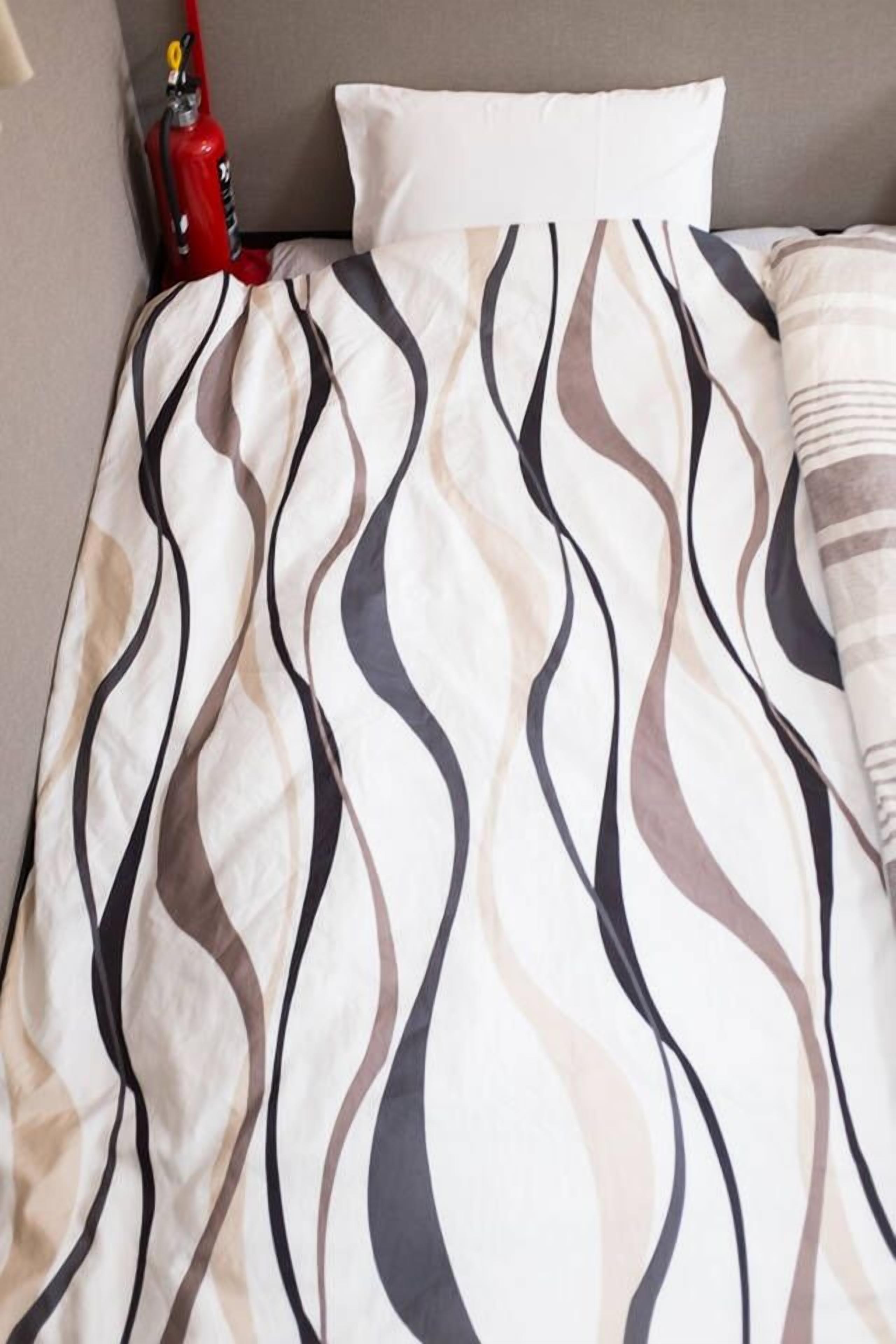 A bed with a patterned bedspread and a red fire extinguisher in the corner.