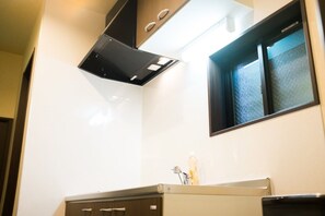 A kitchen with a white backsplash, a window with a view, and a stainless steel range hood. - GH One More Heart at Toji 1 (Kyoto)