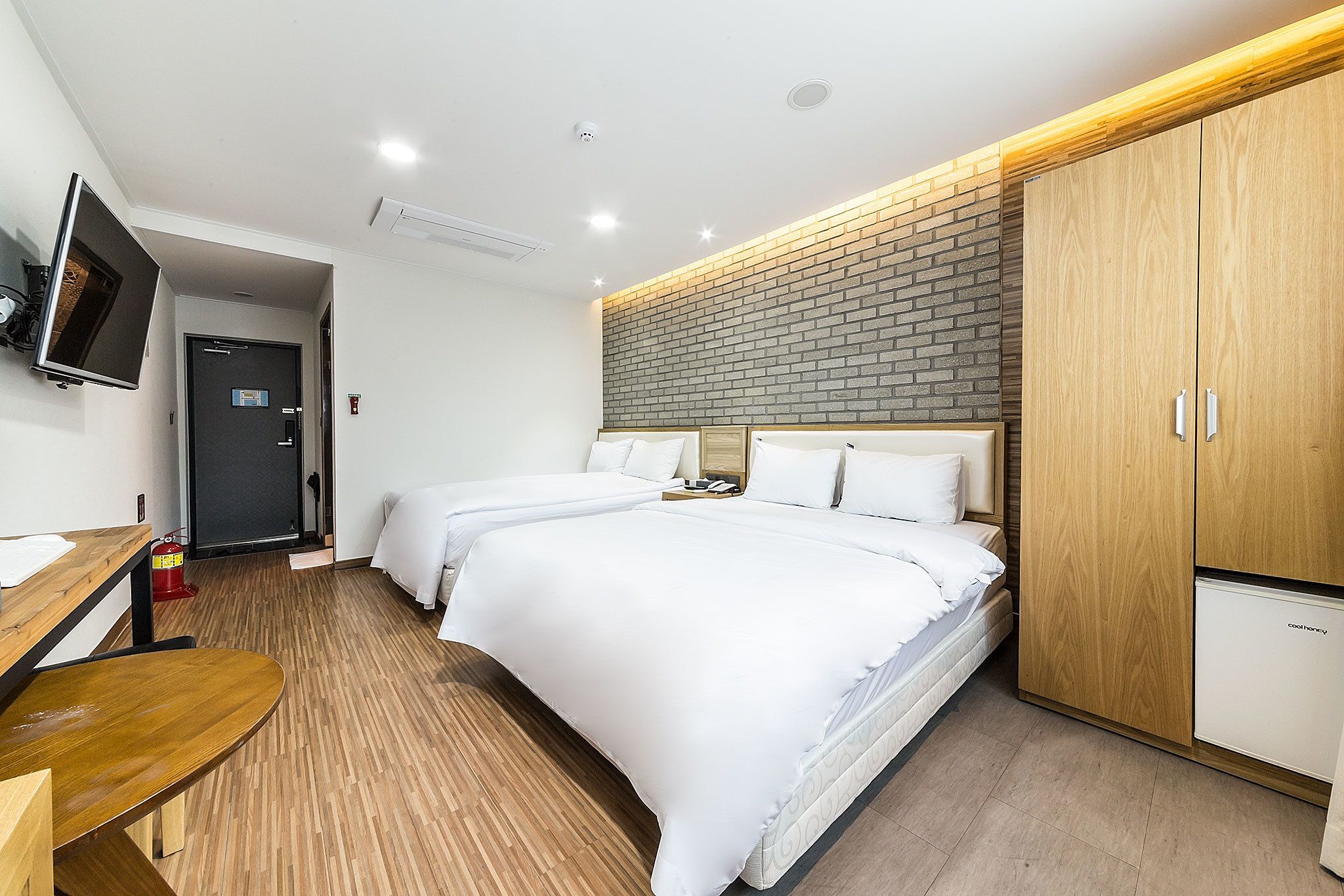 A hotel room with two beds, a wooden desk, a TV, and a wardrobe.