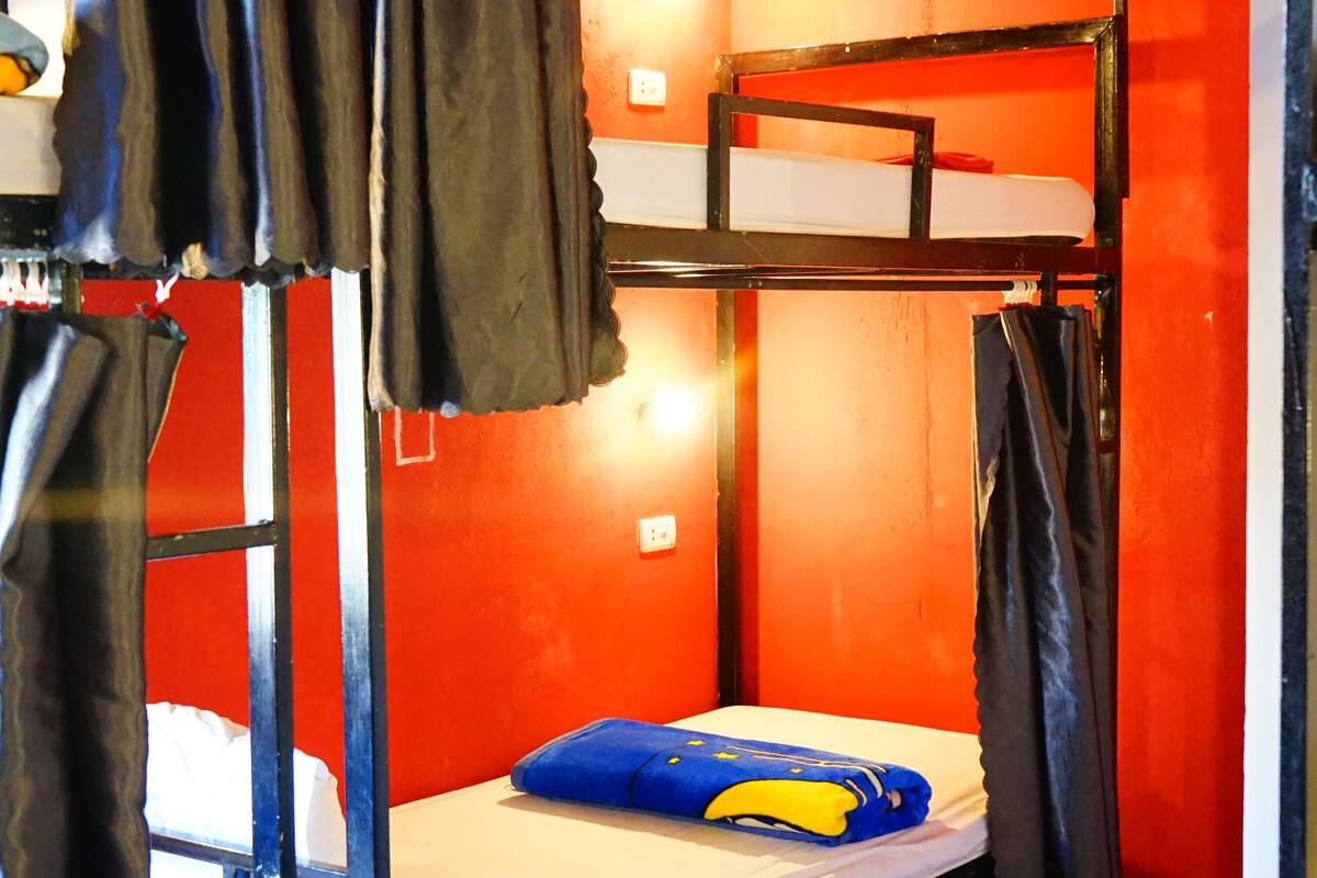 A bunk bed room with a red wall, a white mattress, and a blue pillow.
