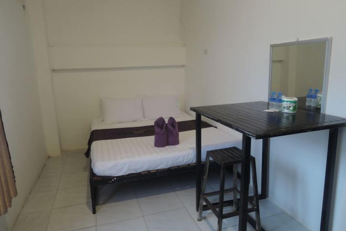 A small, single-room hotel room with a bed, a small table, a stool, and a mirror.