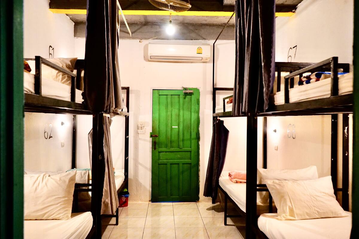 A dormitory room with bunk beds, a green door, and an air conditioning unit on the wall.