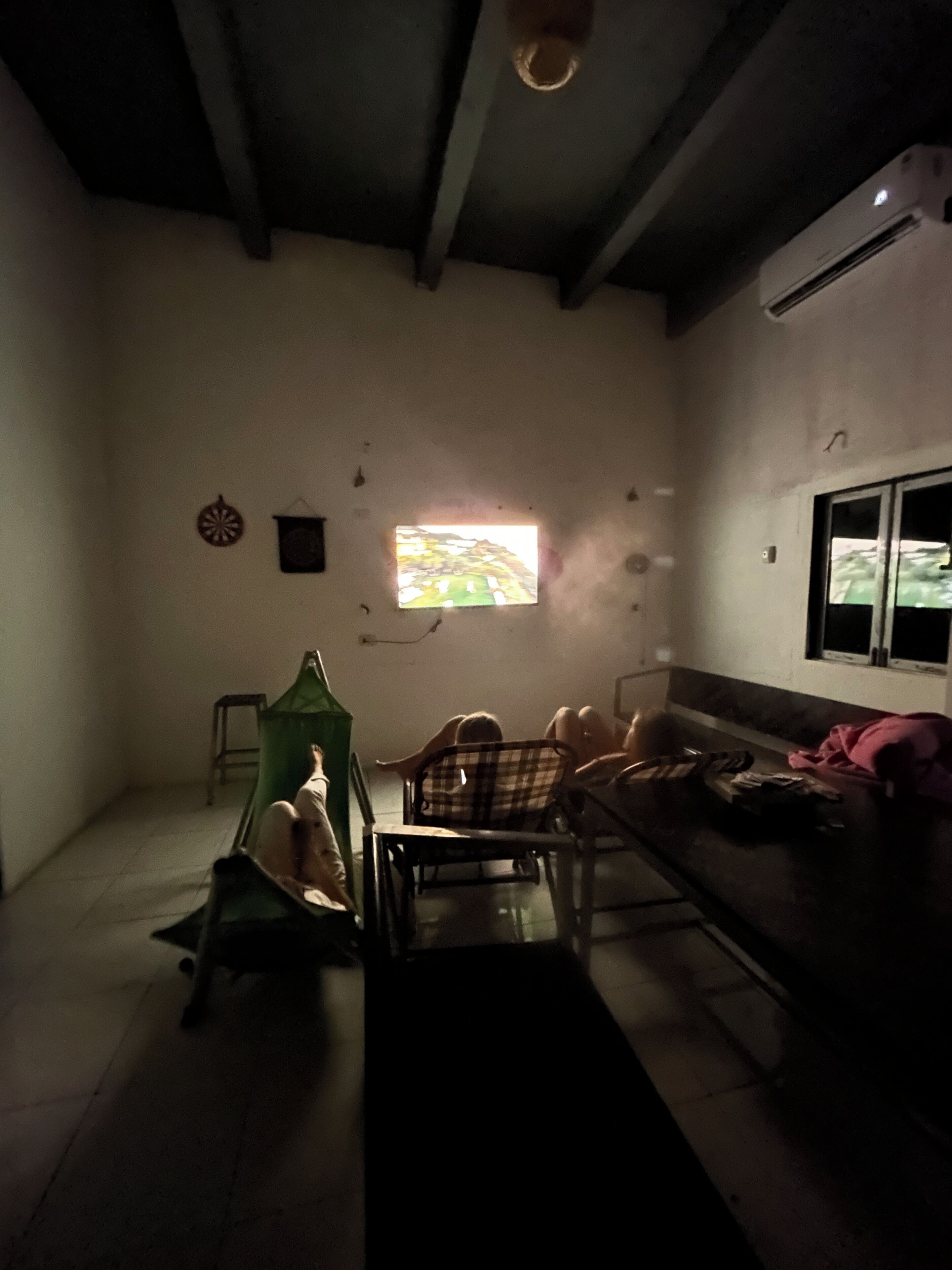 Una habitación con poca luz, una ventana, una silla verde, un sofá y una mesita.