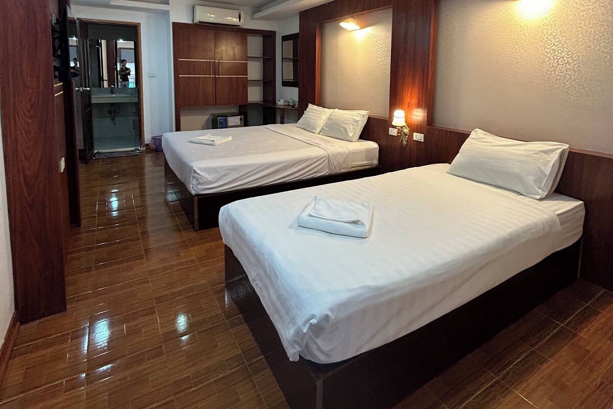 A hotel room with two beds, wooden flooring, a wardrobe, and a bathroom visible in the background.