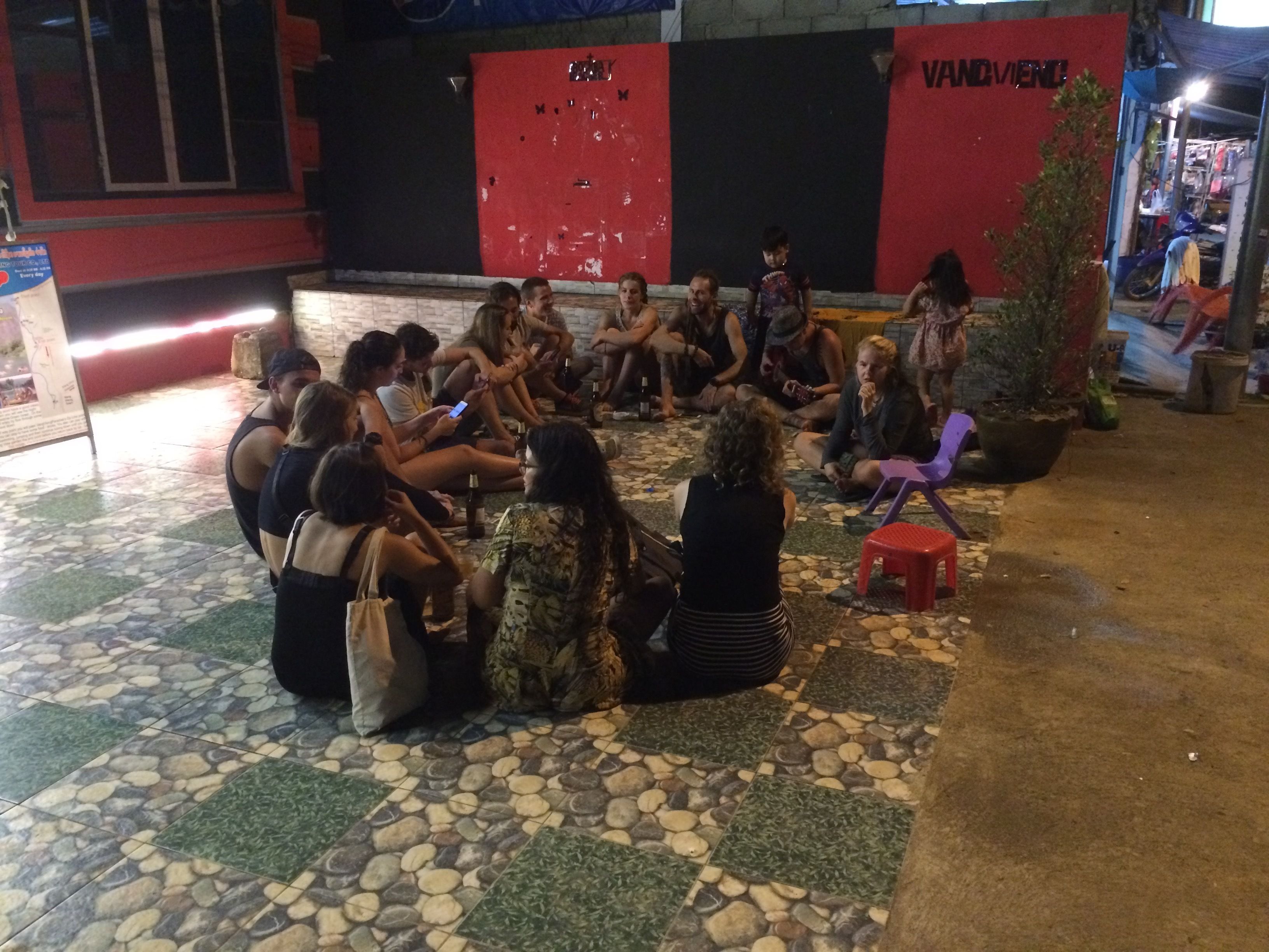A group of people sitting on a tiled floor outdoors, possibly in a courtyard or public space.