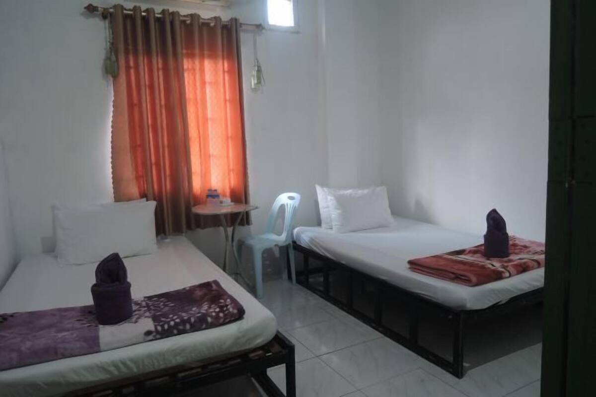 A room with two beds, a small table, a chair, and a window with curtains.