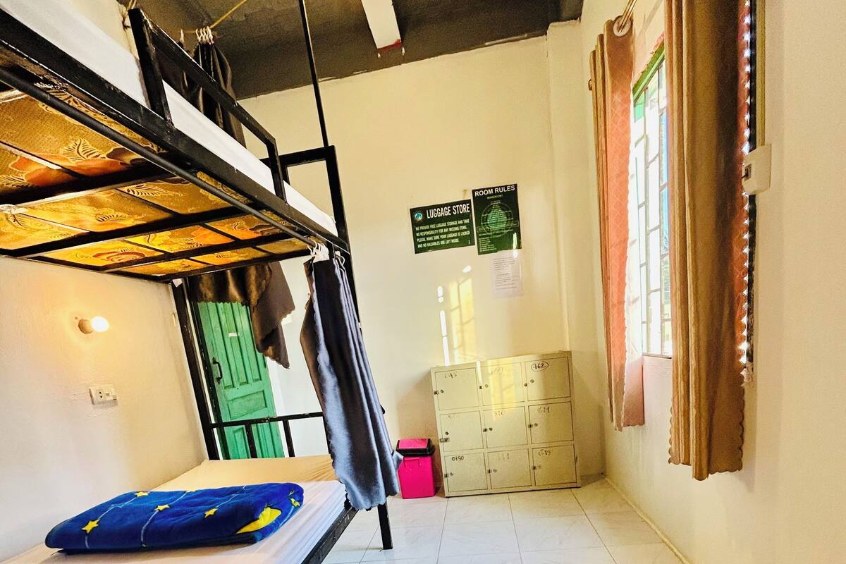 A dormitory room with bunk beds, a green door, a luggage storage area, and a bulletin board with room rules.