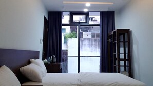 Quarto de hotel com duas camas, um guarda-roupa, uma escrivaninha com cadeira e uma janela com cortinas.