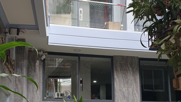 Um edifício moderno com varanda de vidro, uma scooter estacionada e plantas em vasos.