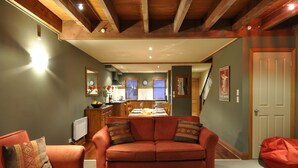 A cozy living room with a red sofa, wooden beams on the ceiling, and a dining area in the background. - Lansdown Peaks Apartments (Wanaka)