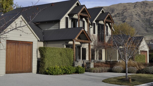 A two-story house with a garage, stone foundation, and a mountain backdrop. - Lansdown Peaks Apartments (Wanaka)