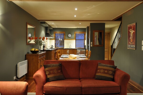 A cozy living room with a red sofa and a dining area with a wooden table and chairs. - Lansdown Peaks Apartments (Wanaka)