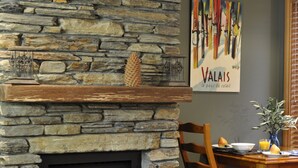 A stone fireplace with a fire, a dining table with chairs, and a painting on the wall. - Lansdown Peaks Apartments (Wanaka)